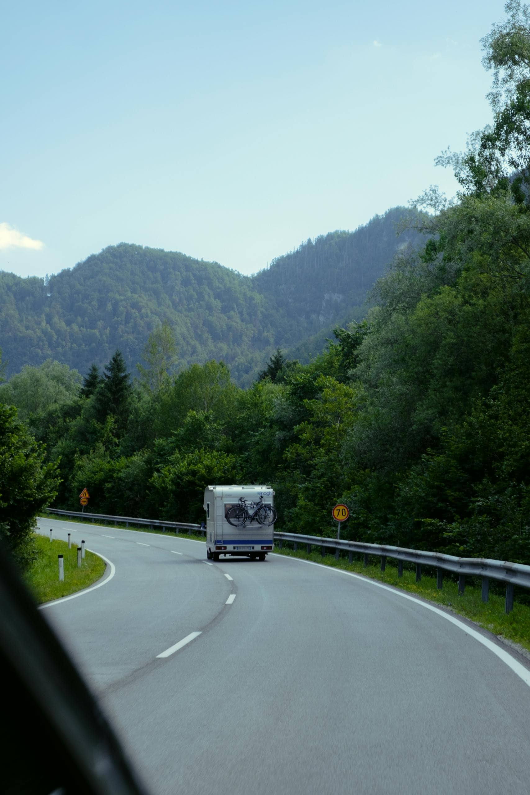 Camper van travels on a winding road surrounded by lush forest and mountains. Perfect travel imagery.