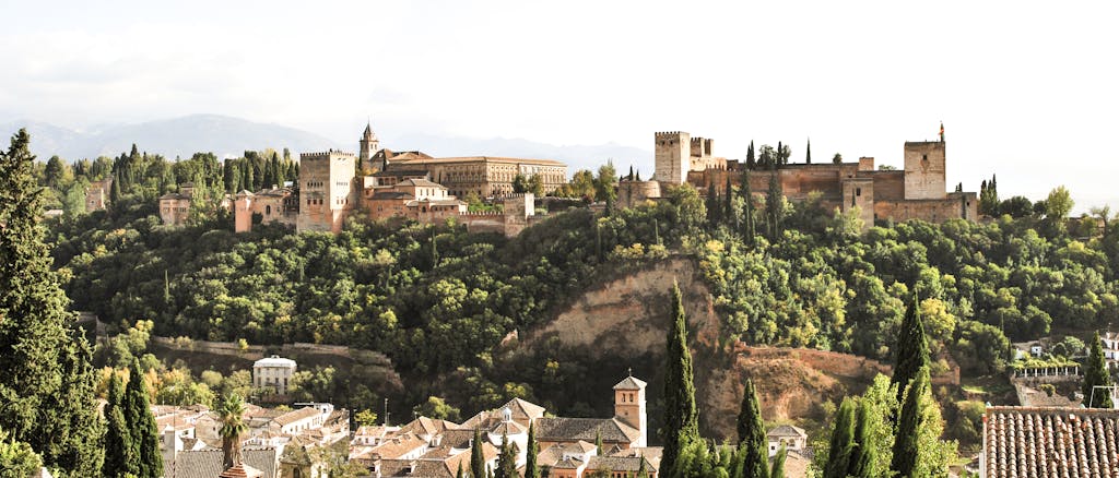 Places to stay in Spain. Scenic view of the historic Alhambra Palace in Granada, Spain surrounded by lush greenery.
